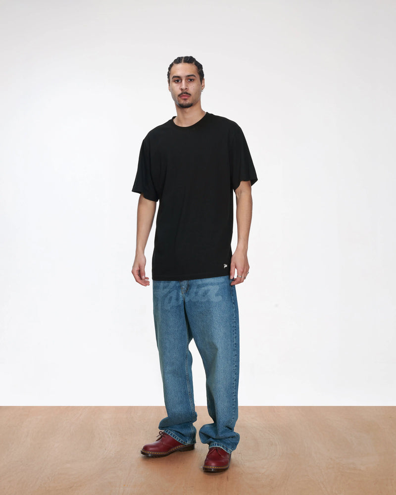 Model wearing a black Patta Tubular T-Shirt with relaxed blue jeans on a white backdrop.