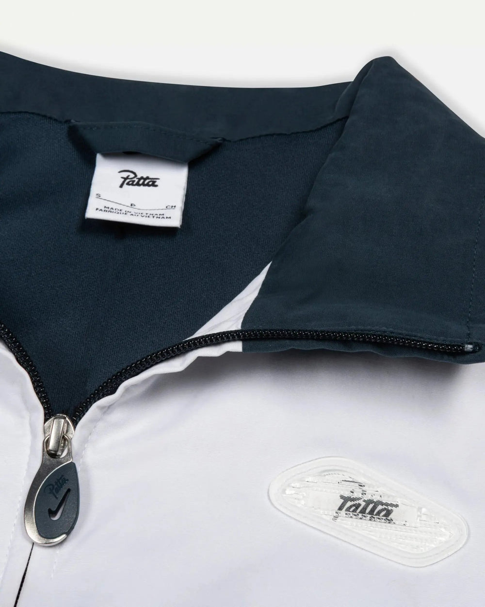 Detail of the Patta x Nike NRG Track Jacket collar, custom zipper pull, and chest badge in deep ocean and white.
